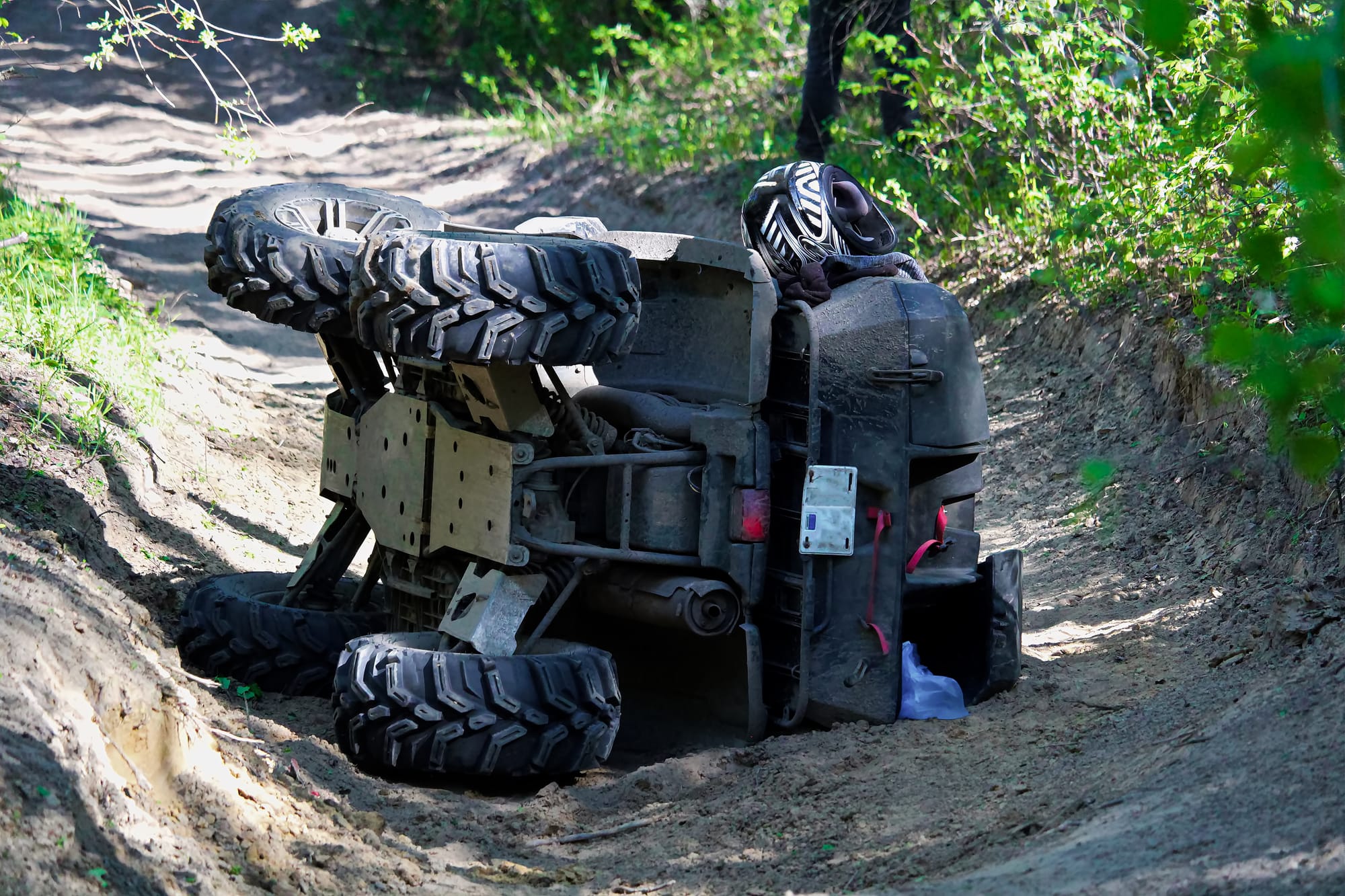 An ATV flipped over on its side in the middle of a dirt trail.