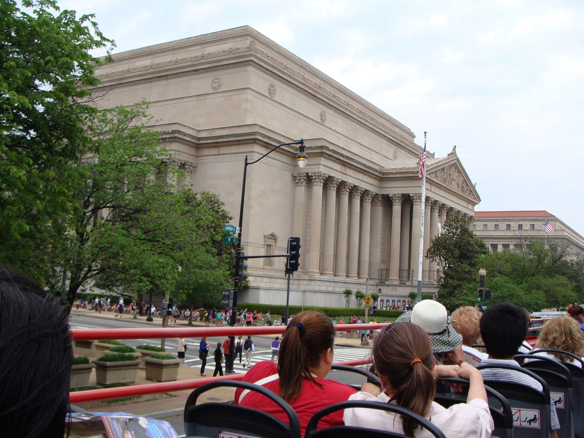 An open-air tour bus on the streets of Washington DC with people sitting on the bus sightseeeing.