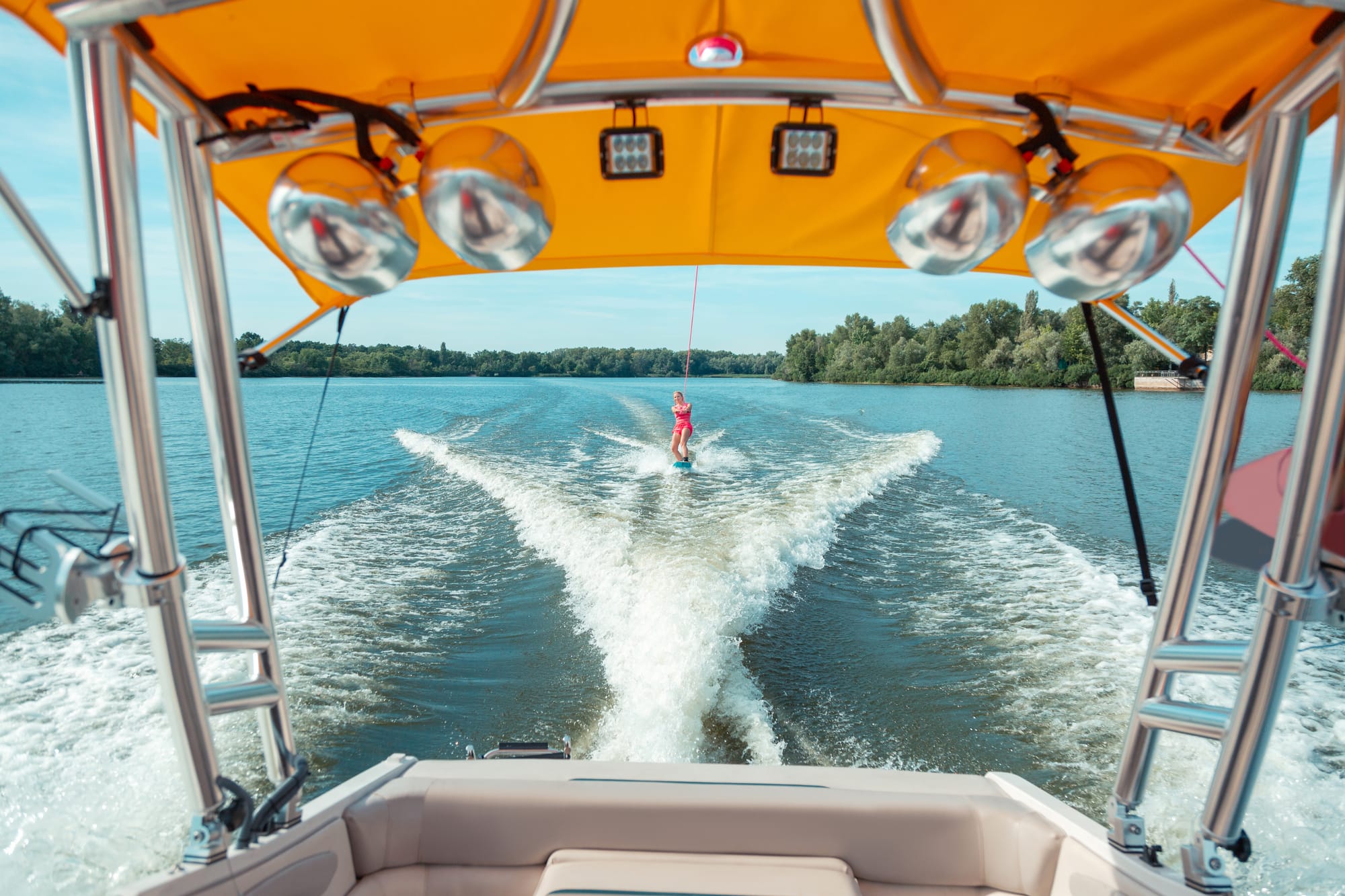 A long-haired girl in pink shorts and a life jacket wakeboarding behind a boat.
