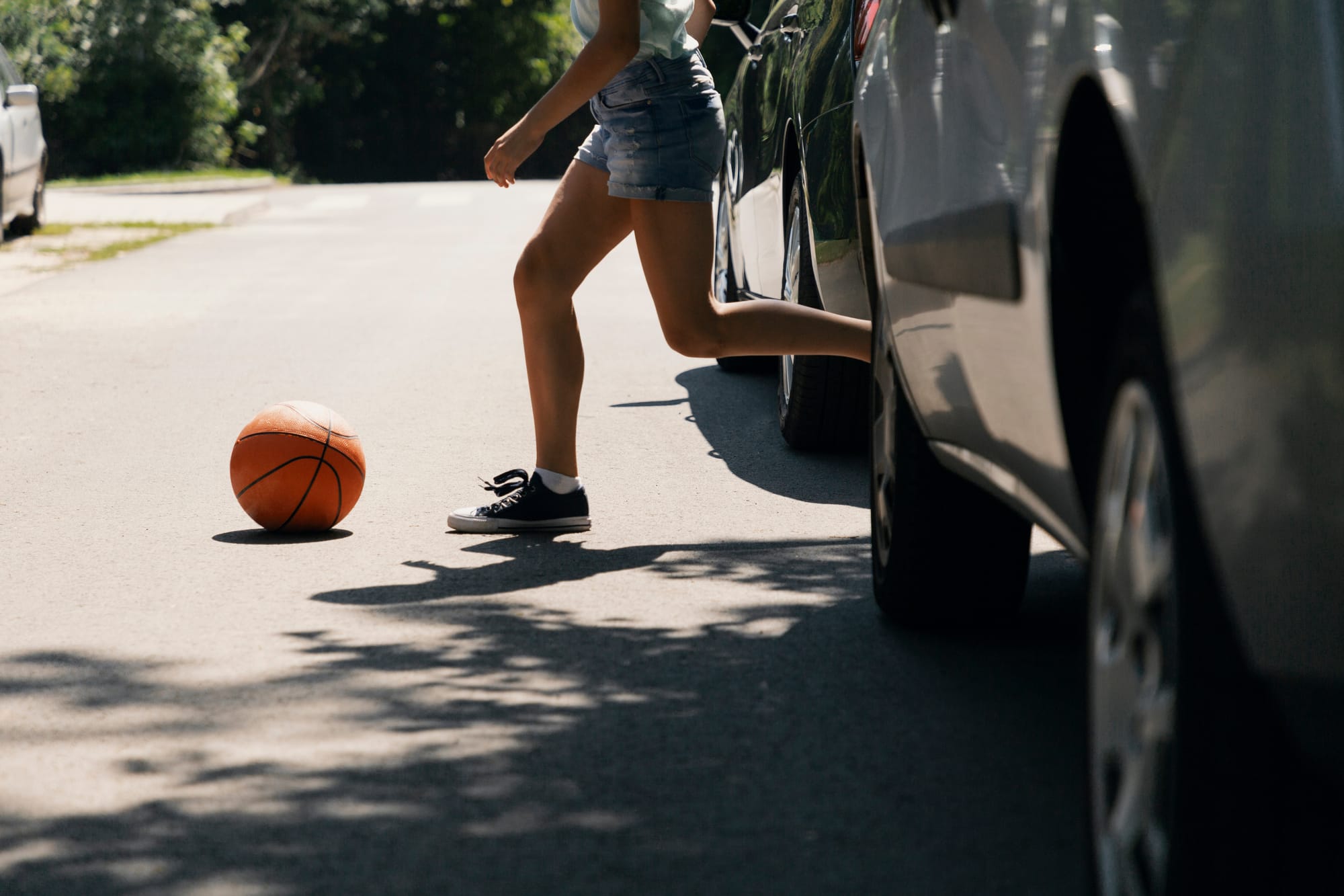 Girl running into the street chasing a ball next to parked cars.