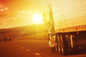 semi truck driving on road towards sun